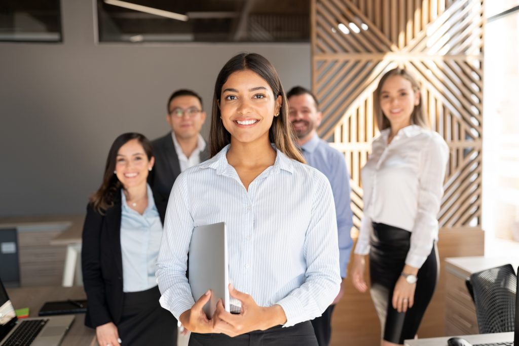 Woman smiling with laptop with coworkers in background